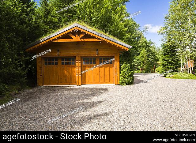 Golden-brown stained piece sur piece Eastern white pine log and timber 2 car garage with carved wood details and Gramineae or Poaceae - Grass and Bryophyta -...
