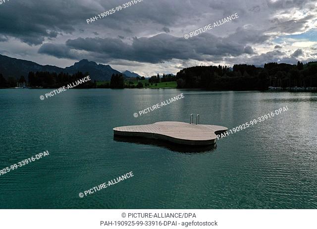 25 September 2019, Bavaria: Under dense clouds a deserted bathing platform floats on the Forggensee (aerial photograph with a drone)