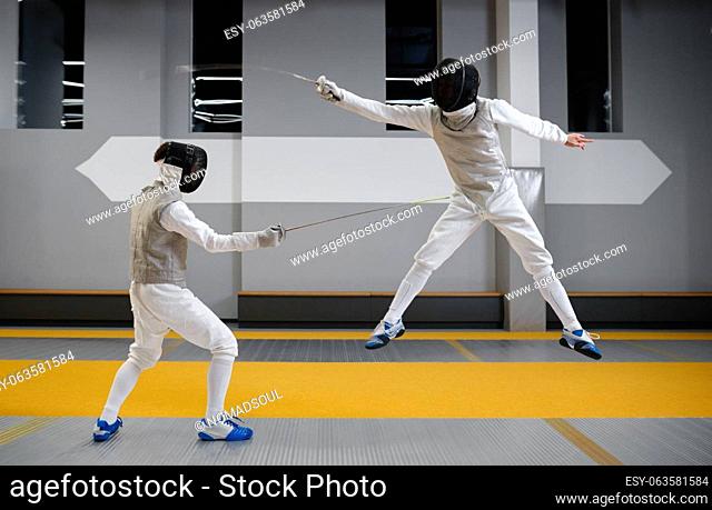 Two fencers sparring during training session in professional martial art school. Swordsman jumping trying to dodge an attack