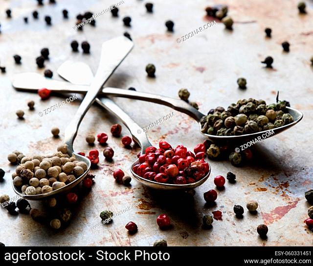 different color peppercorn seeds on vintage spoons on steel plate