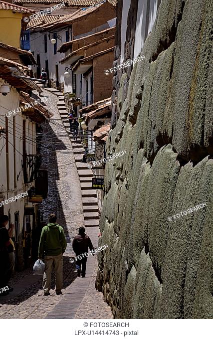 Cuzco: street scene on steep road to San Blas, cobbled street with steps, houses of stone, and white stucco, massive Inca stone wall in foreground, Cuzco
