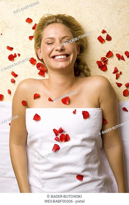 Germany, young woman lying on massage table, petals on chest