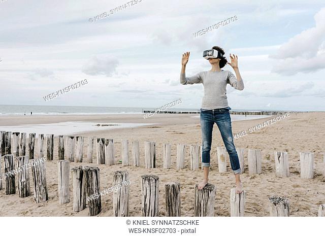 Woman standing on wooden stakes on the beach wearing VR glasses