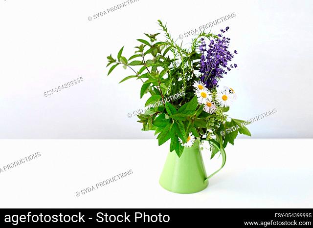 bunch of herbs and flowers in green jug on table
