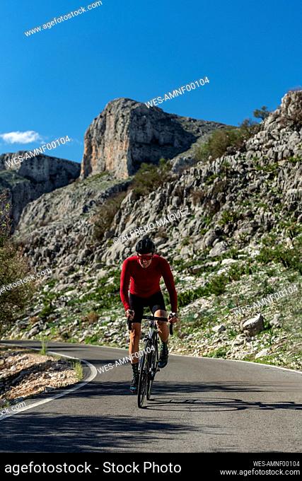 Mature cyclist wearing helmet riding bicycle in front of rocks under sky