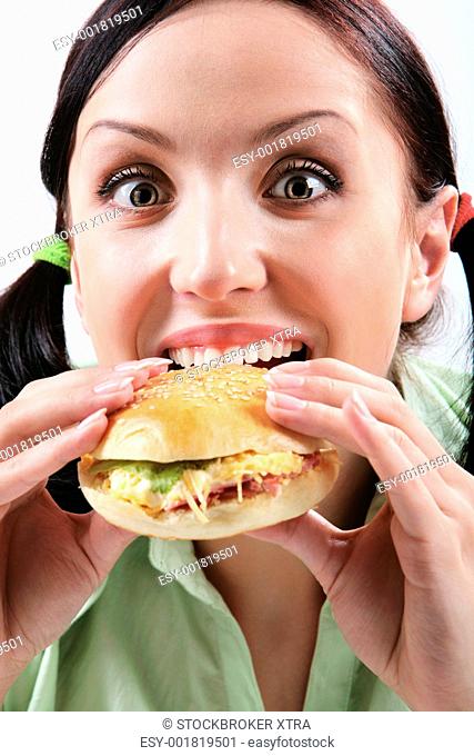 Image of hungry girl eating hamburger and looking at camera