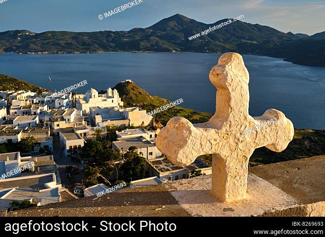 Greek Orthodox Christianity concept background, Christian cross with Plaka village on Milos island in background on sunset, Plaka town, Milos island, Greece