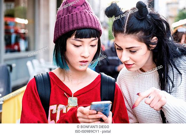 Two young stylish women looking at smartphone on city street
