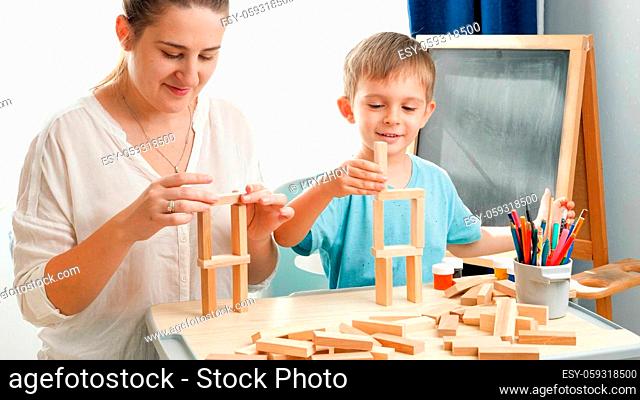 Little boy with mother laughing after high toy wooden blocks tower falling. Mother educating and teaching her child at home during lockdown and self isolation