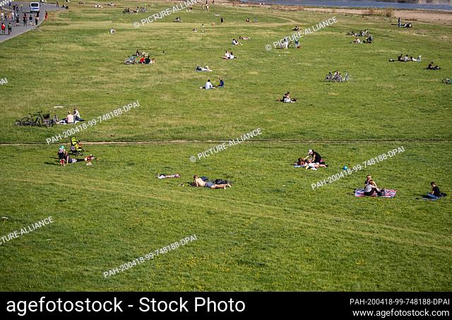 18 April 2020, Saxony, Dresden: People lie at intervals on the Elbe meadows. In the Free State of Saxony, slightly relaxed restrictions on public life will...