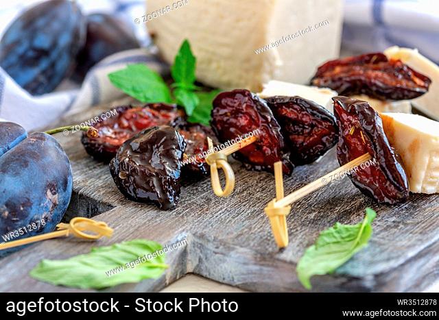 Appetizer of homemade cheese and dried plums on a wooden serving board, selective focus