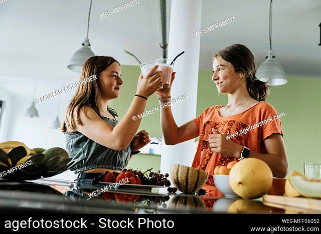 Teenage girls standing in kitchen tasting with fresh fruit smoothies