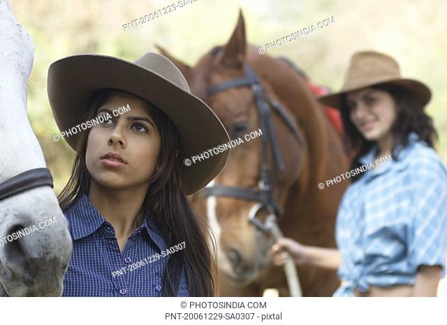 Young woman and a teenage girl standing with two horses
