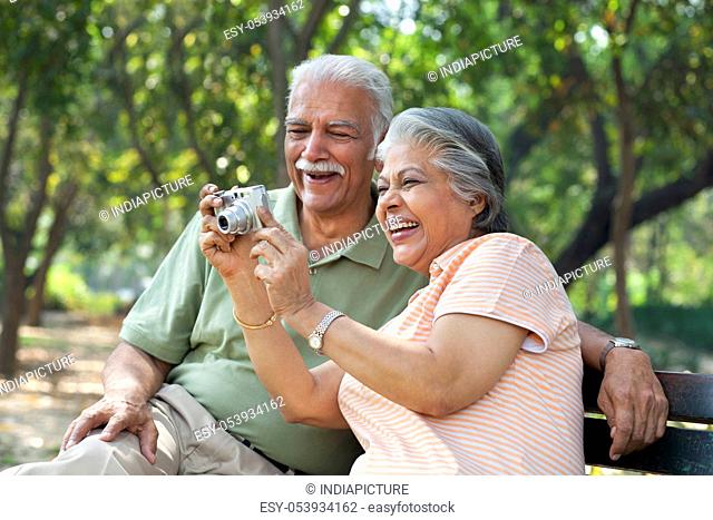 Smiling couple using digital camera at park