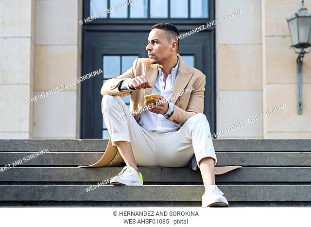 Businessman with smartphone sitting on stairs in the city