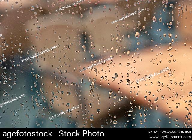 29 July 2023, Saxony-Anhalt, Wernigerode: Raindrops collect on a glass pane on the market square, in the background the exterior of a cafe