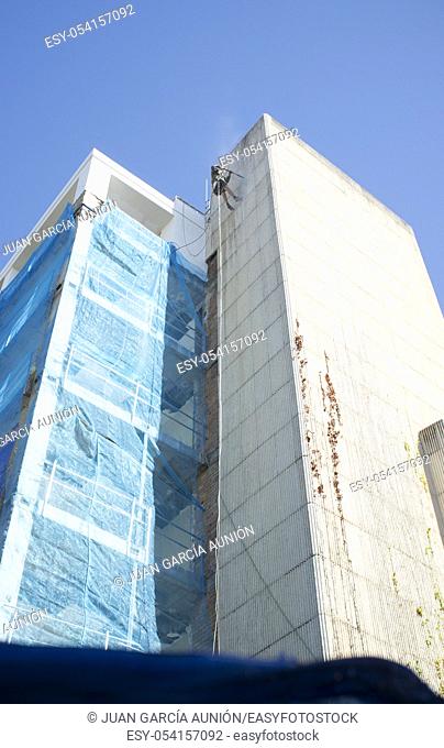 Rope access technician washing building facade. Cleaning service at height concept. Córdoba, Spain