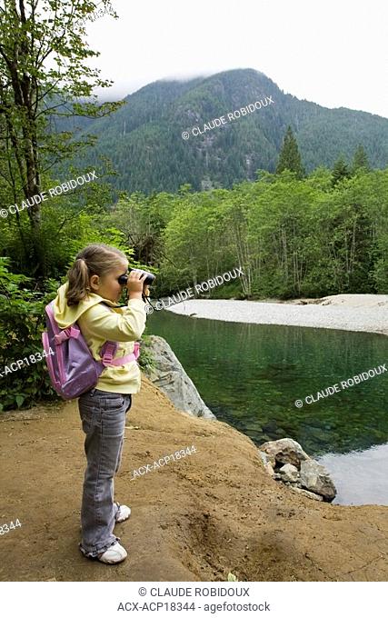 Little girl looking through binoculars on a hiking trail at Golden Ears Provincial Park in Maple Ridge, British Columbia, Canada