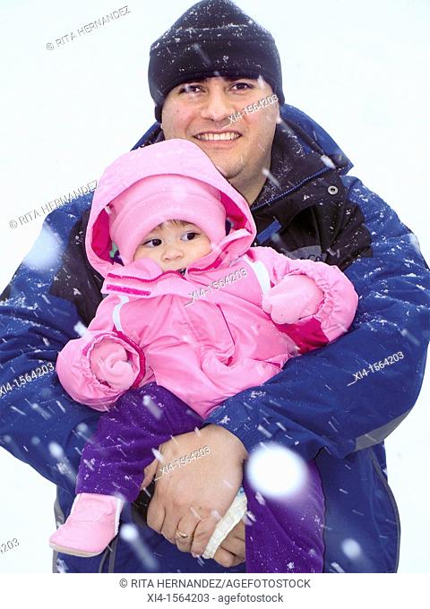 Smiling father holding baby under snow storm. Baby in the snow