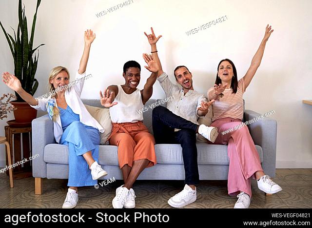Male and female coworkers cheering while sitting on sofa