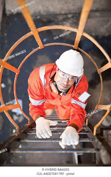 Worker climbing ladder at oil refinery