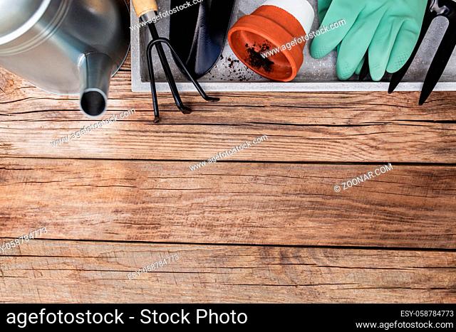 Gardening hobby concept flat lay with ceramic pot, pitchfork, shovel, gloves, metal watering can and dirt on wooden background