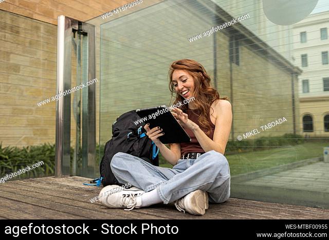 Woman smiling while using digital tablet by backpack