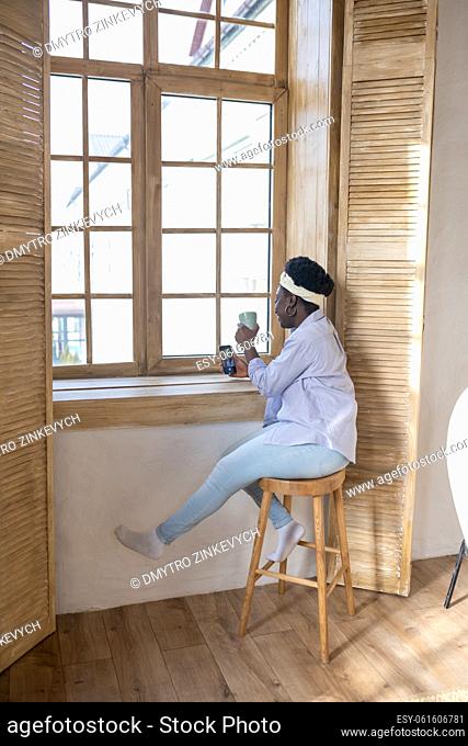 At the window. African woman with a smartphone sitting near the window