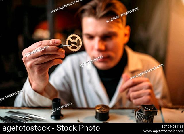 Watchmaker holding with tweezers a gear of old hours. Broken mechanical watches repairing