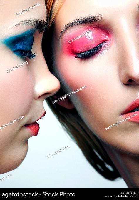 Two young women with blue and pink smoky eues makeup and glossy glitter skin. Closeup shot of blonde and brunette girls. Female friendship concept
