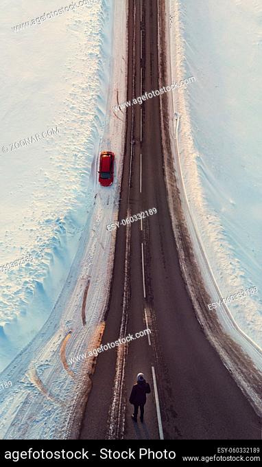 Surreal image with an unusual perspective with a woman on a winter road and car, simultaneous top view and normal view