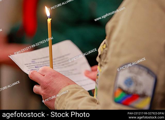 17 December 2023, Saxony-Anhalt, Halberstadt: A participant in an ecumenical service holds a candle symbolizing the Light of Peace from Bethlehem in St
