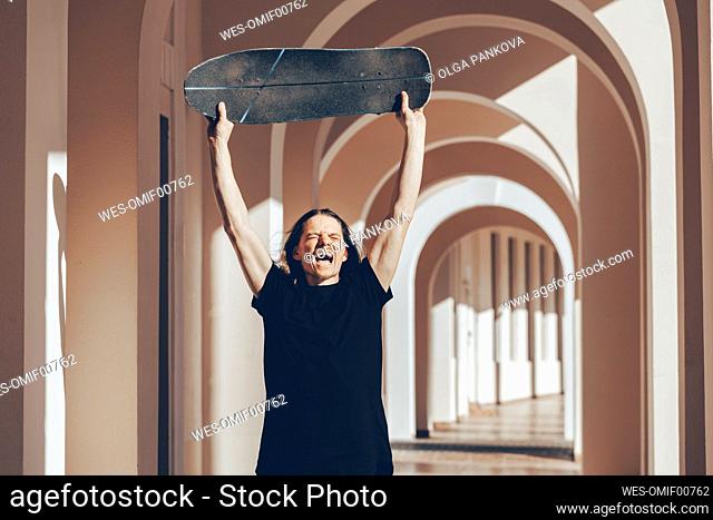 Man lifting skateboard above head shouting in arcade