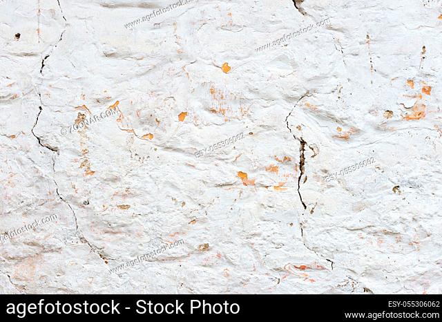 Textured grunge background. Volumetric plastered wall with a multilayer cracked coating. Orange chips on the whitewashed wall