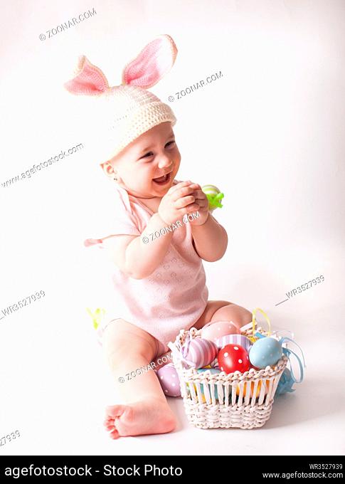 Cute baby girl sitting in a knitted rabbit hat isolated on white