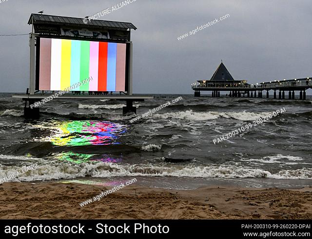 06 March 2020, Mecklenburg-Western Pomerania, Heringsdorf: The light of an LED video wall is reflected in the water of the Baltic Sea at the pier in the evening...