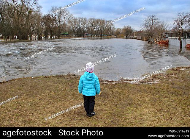 Child watching river flooding in city after melting snow in spring. Natural disaster. Flooding of river in spring during melting of snow. Spring flood