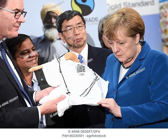 German Chancellor Angela Merkel (R) looks at a fair trade t-shirt next to German development aid minister Gerd Mueller (L-R)
