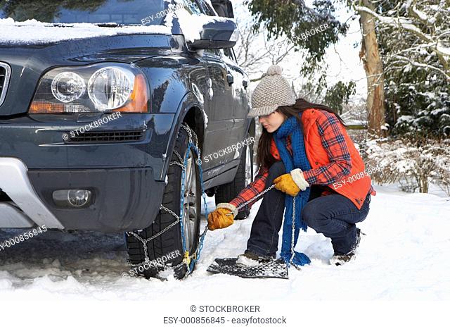 Woman Putting Snow Chains Onto Tyre Of Car