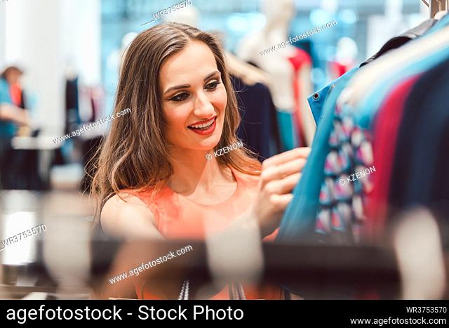 Woman browsing through dresses on rack in fashion store looking happy