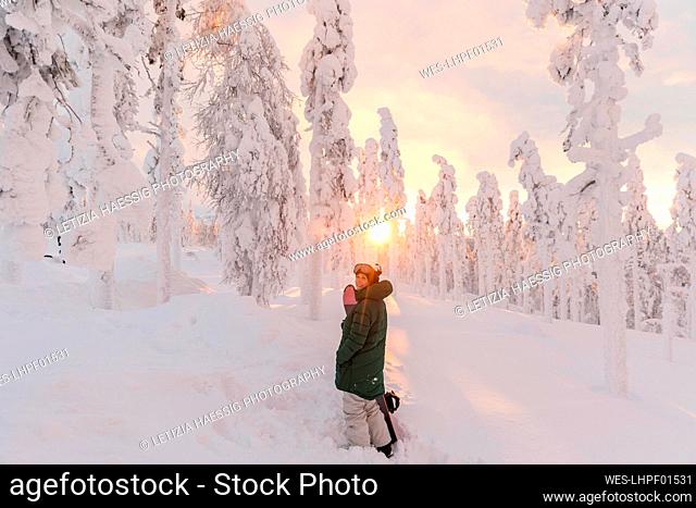 Woman with snowboard standing on snow-covered field during sunrise