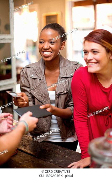 Two female friends paying bill in cafe
