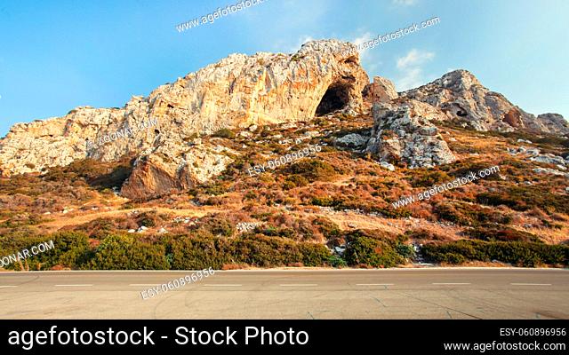 Evening sun shines on typical landscape at Karpass region of Northern Cyprus, small rocky formations by asphalt road.