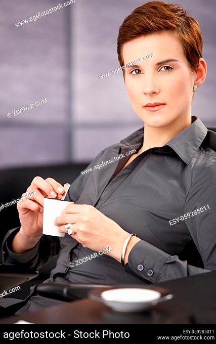 Portrait of serious businesswoman having coffee, holding cup, looking at camera