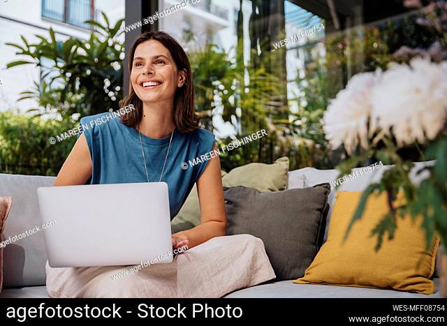 Smiling freelancer with laptop sitting on sofa