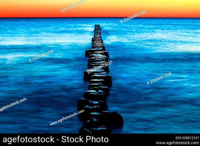 Wooden spur dykes in coastal sunset. Old groynes and wavy sea water, Baltic Sea, Island of Hiddensee, Germany