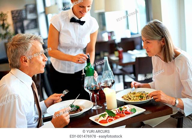 Mature caucasian couple dining in restaurant with a waitress serving wine
