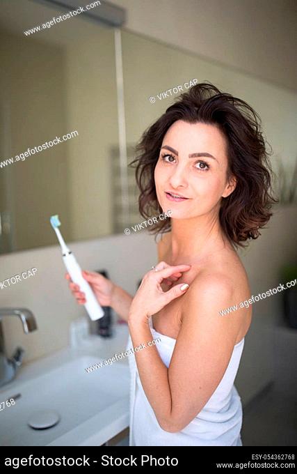 Pretty, middle aged woman brushing her teeth in a modern design bathroom