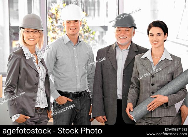 Confident team of architects wearing hardhat, holding plan, smiling at camera