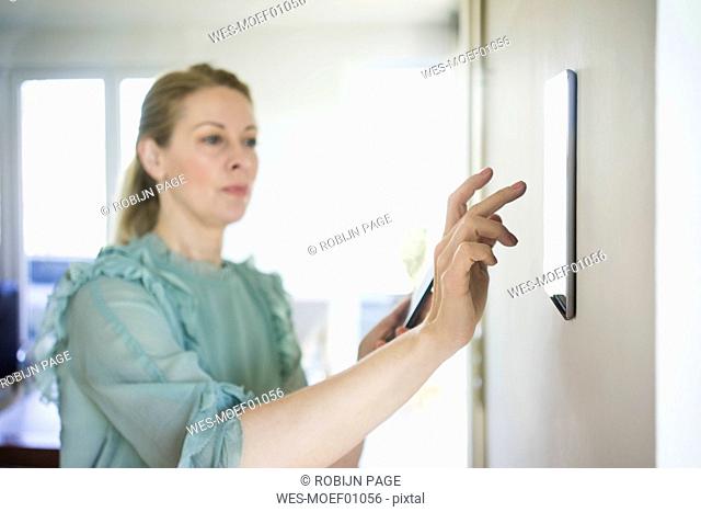 Woman adjusting digital tablet mounted on wall with smartphone